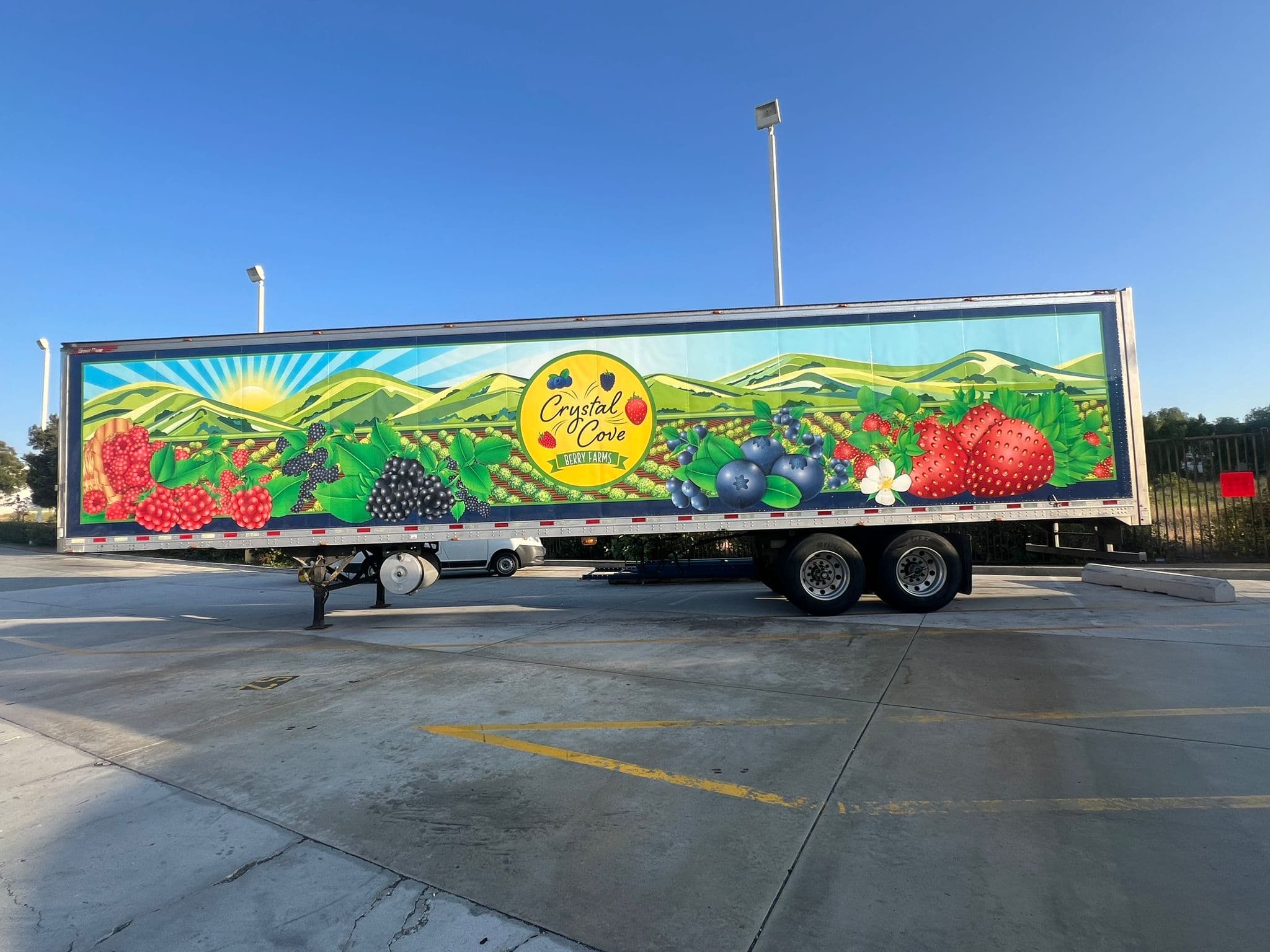 Refrigerated trailer wrapped with an illustrated berry field, rolling hills and a sunrise, with a circular Crystal Cove logo at centre