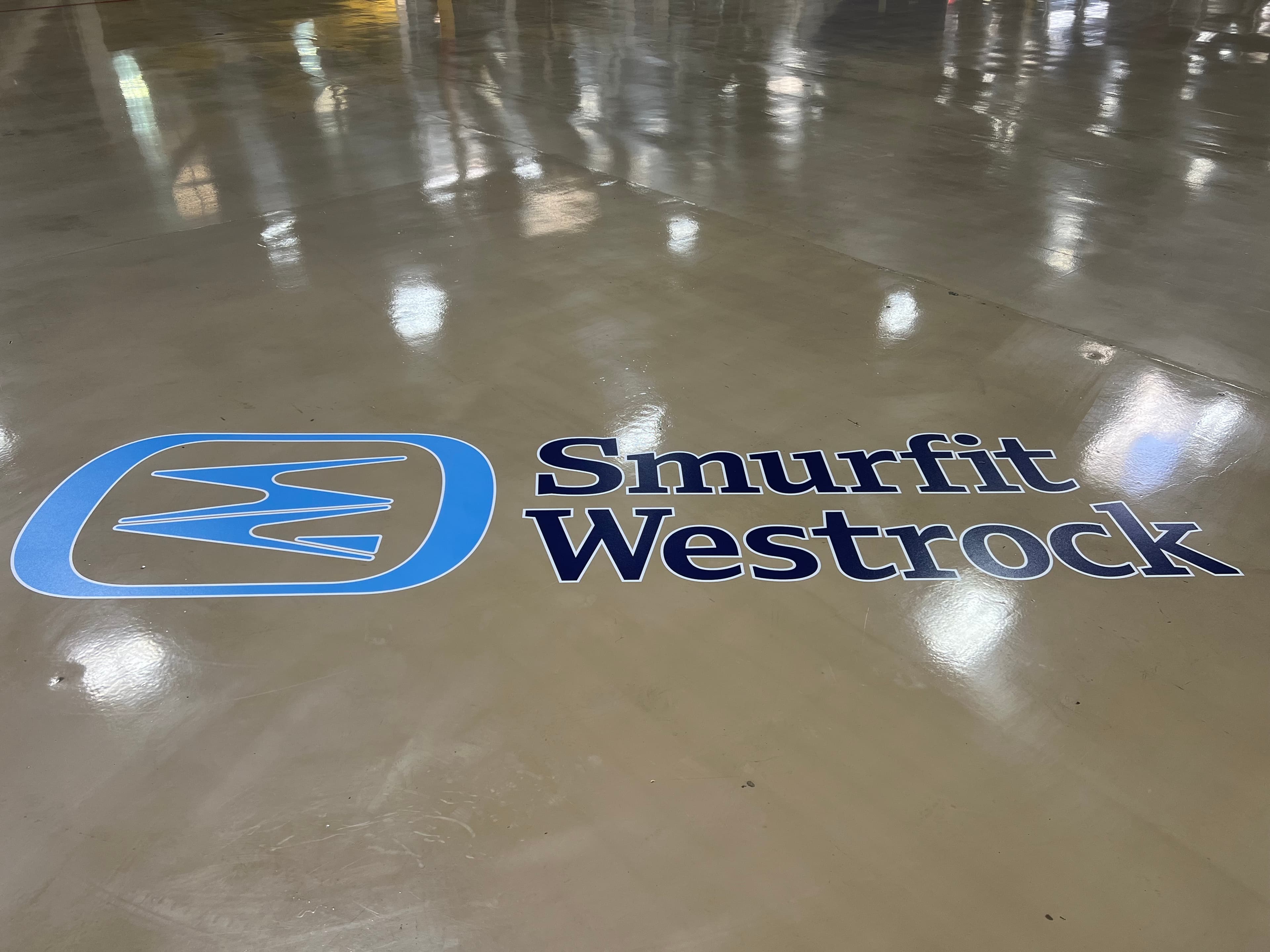 Large Smurfit Westrock logo and wordmark decal applied to a polished concrete warehouse floor