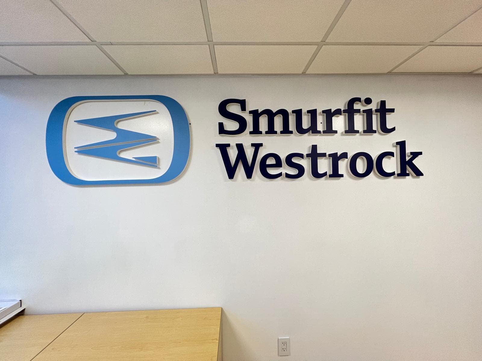 Dimensional acrylic Smurfit Westrock logo and lettering mounted on a white office wall above a wooden desk