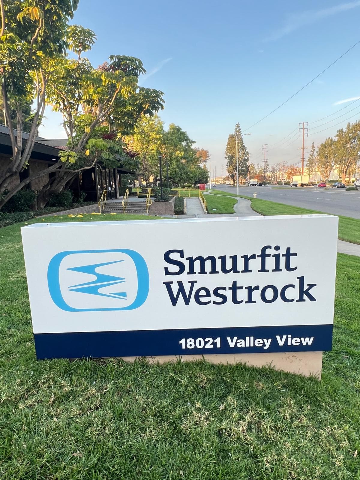 White and navy monument sign on a lawn reading Smurfit Westrock, 18021 Valley View, in front of a low office building