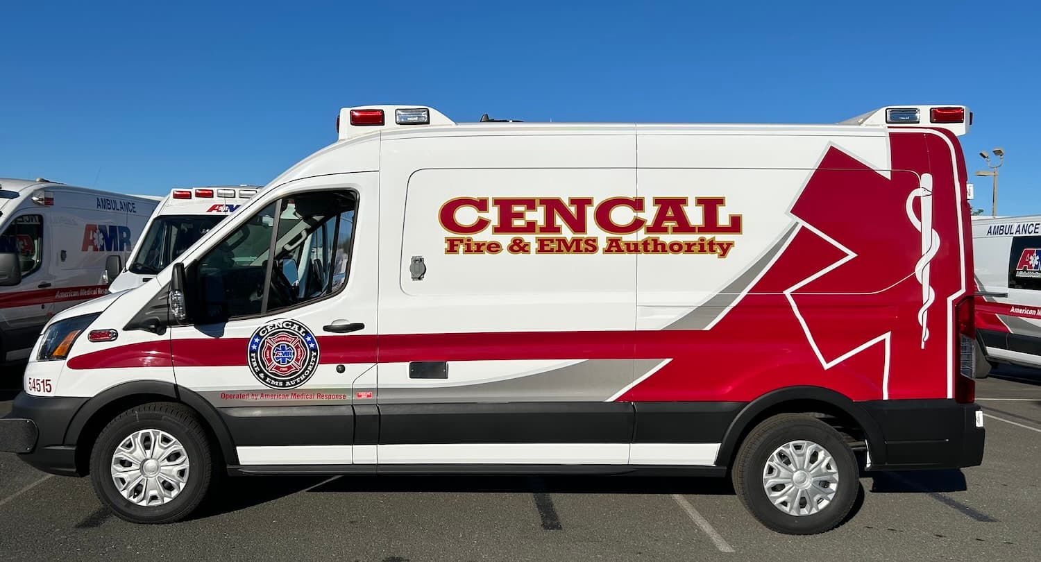 Side view of a white ambulance van with CENCAL Fire & EMS Authority lettering, a red and silver stripe, the authority seal on the driver door and a red star of life on the rear panels