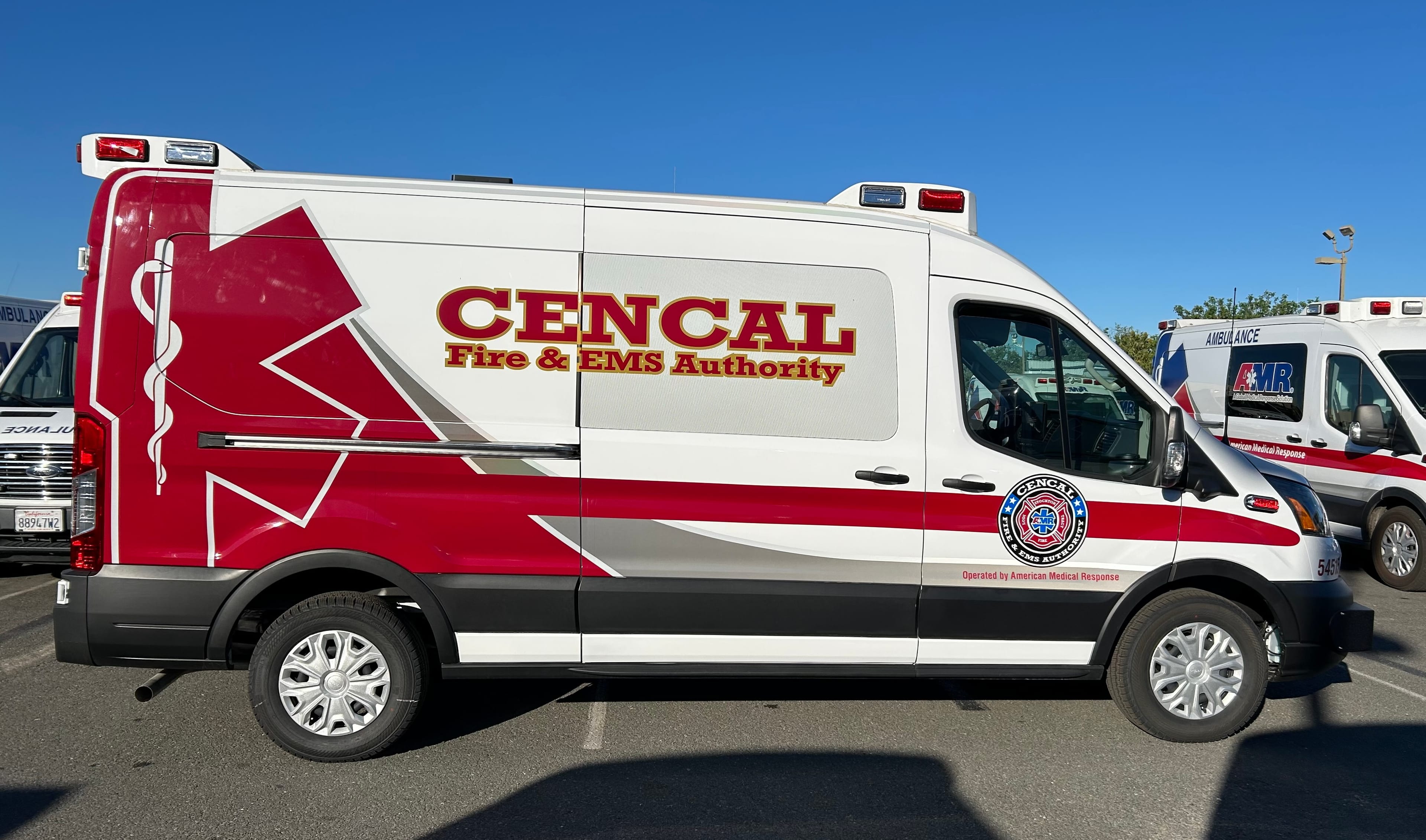 White high-roof ambulance van with CENCAL Fire & EMS Authority lettering in red and gold, a large red star of life across the rear panels and the authority seal on the passenger door, parked beside AMR ambulances