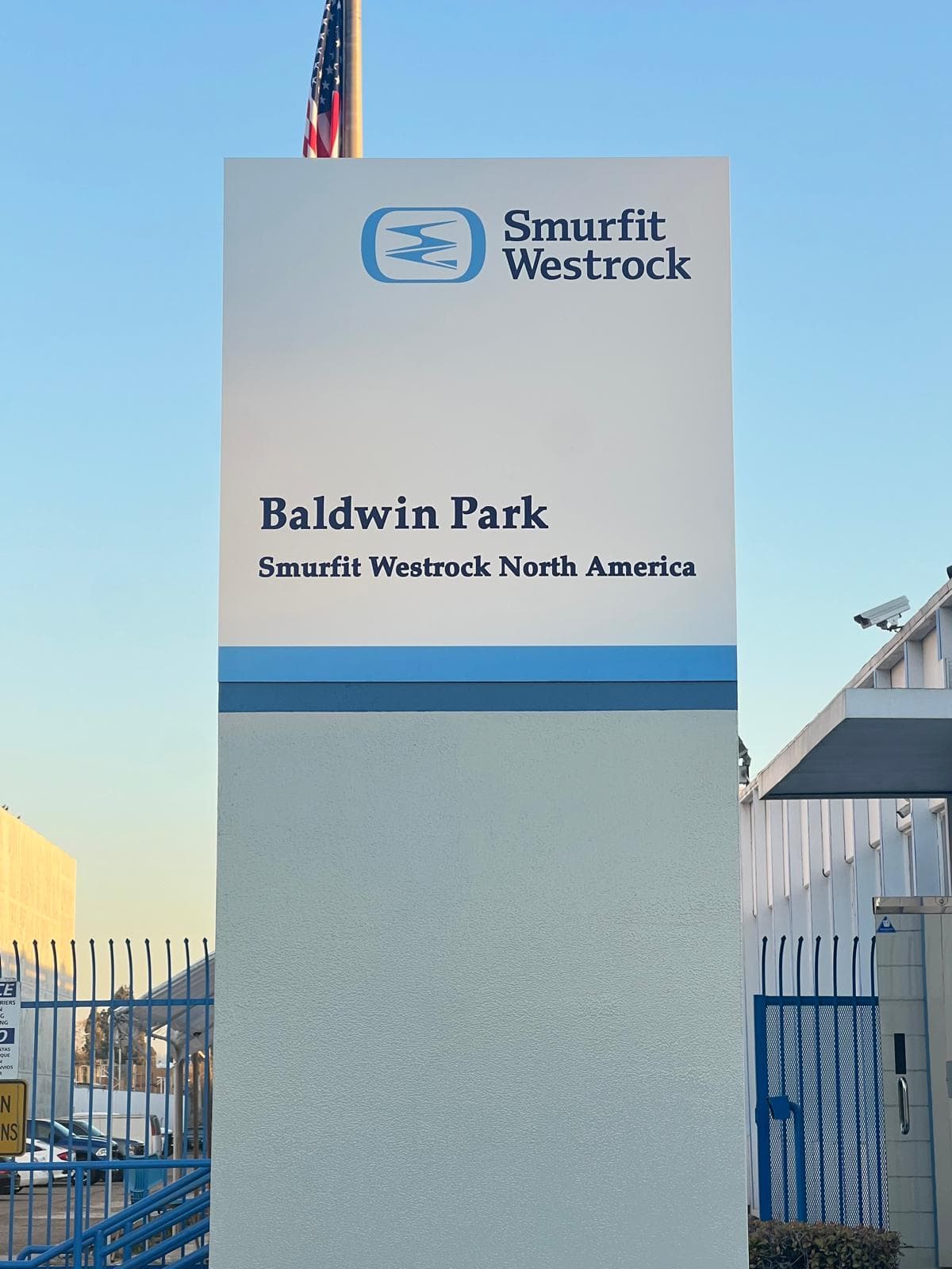 Tall white pylon sign carrying the Smurfit Westrock logo, the words Baldwin Park and Smurfit Westrock North America, with a US flag behind it