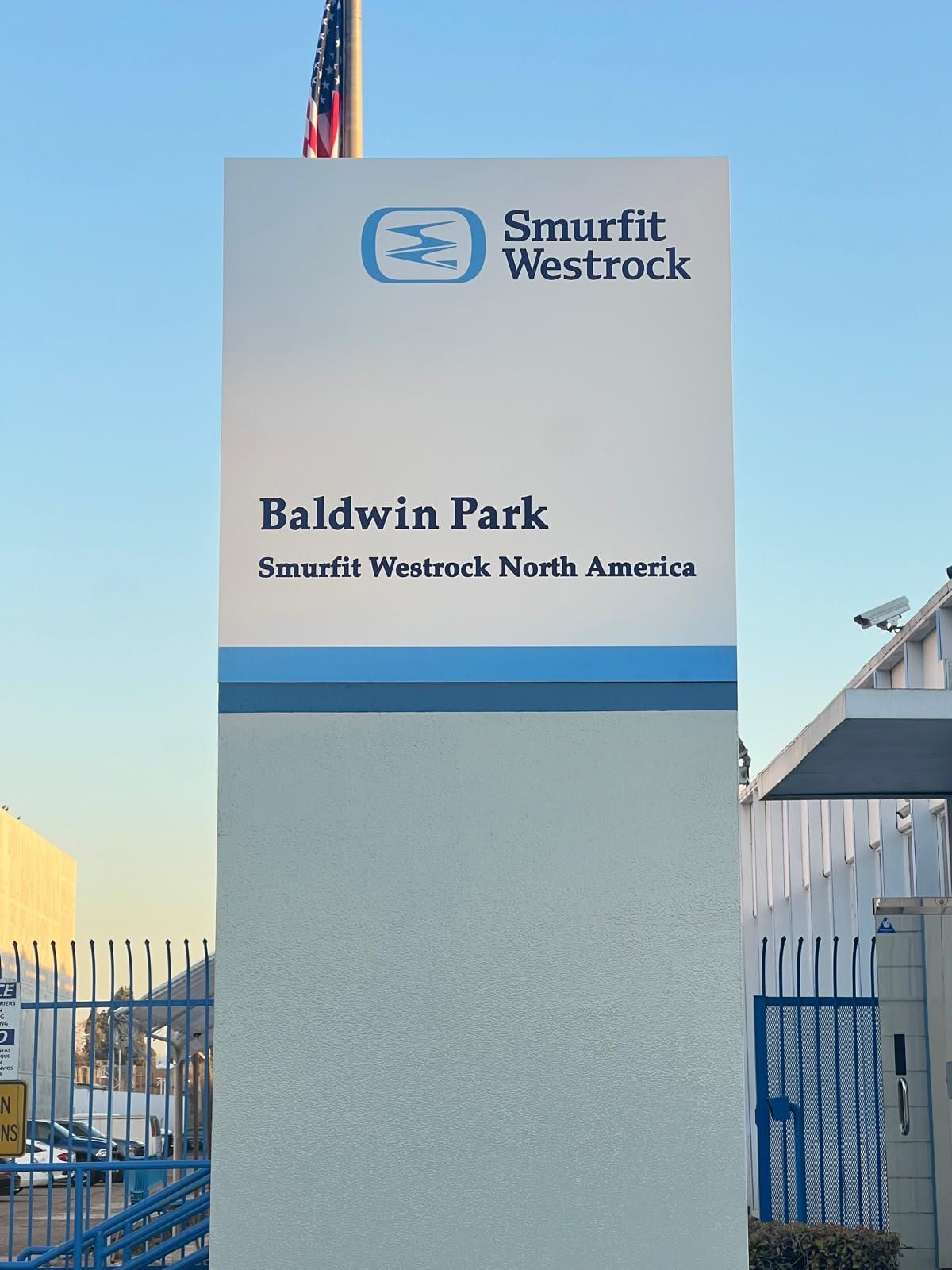 Tall white pylon sign carrying the Smurfit Westrock logo, the words Baldwin Park and Smurfit Westrock North America, with a US flag behind it