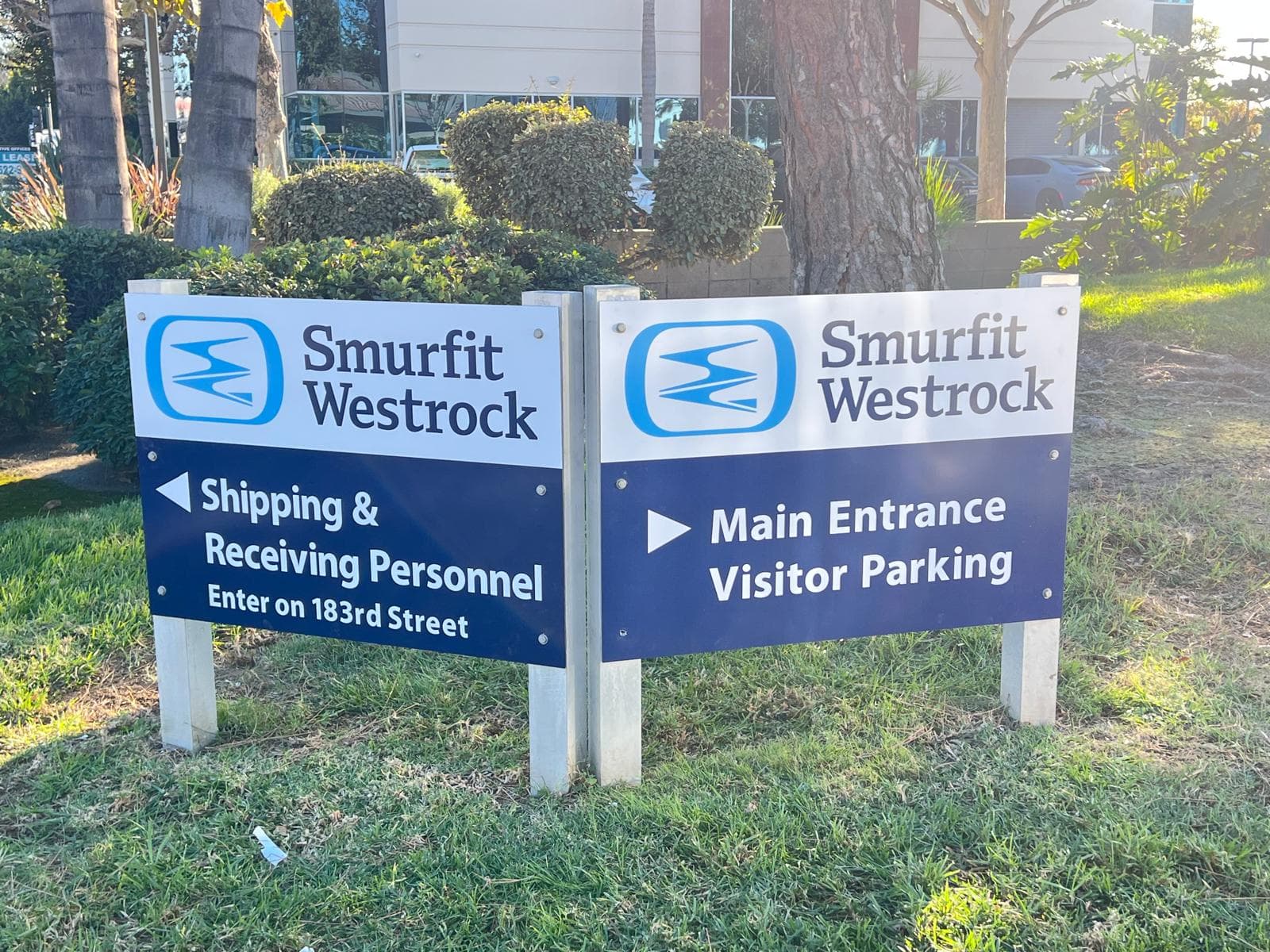 Two post-mounted navy and white wayfinding signs reading Shipping and Receiving Personnel and Main Entrance Visitor Parking