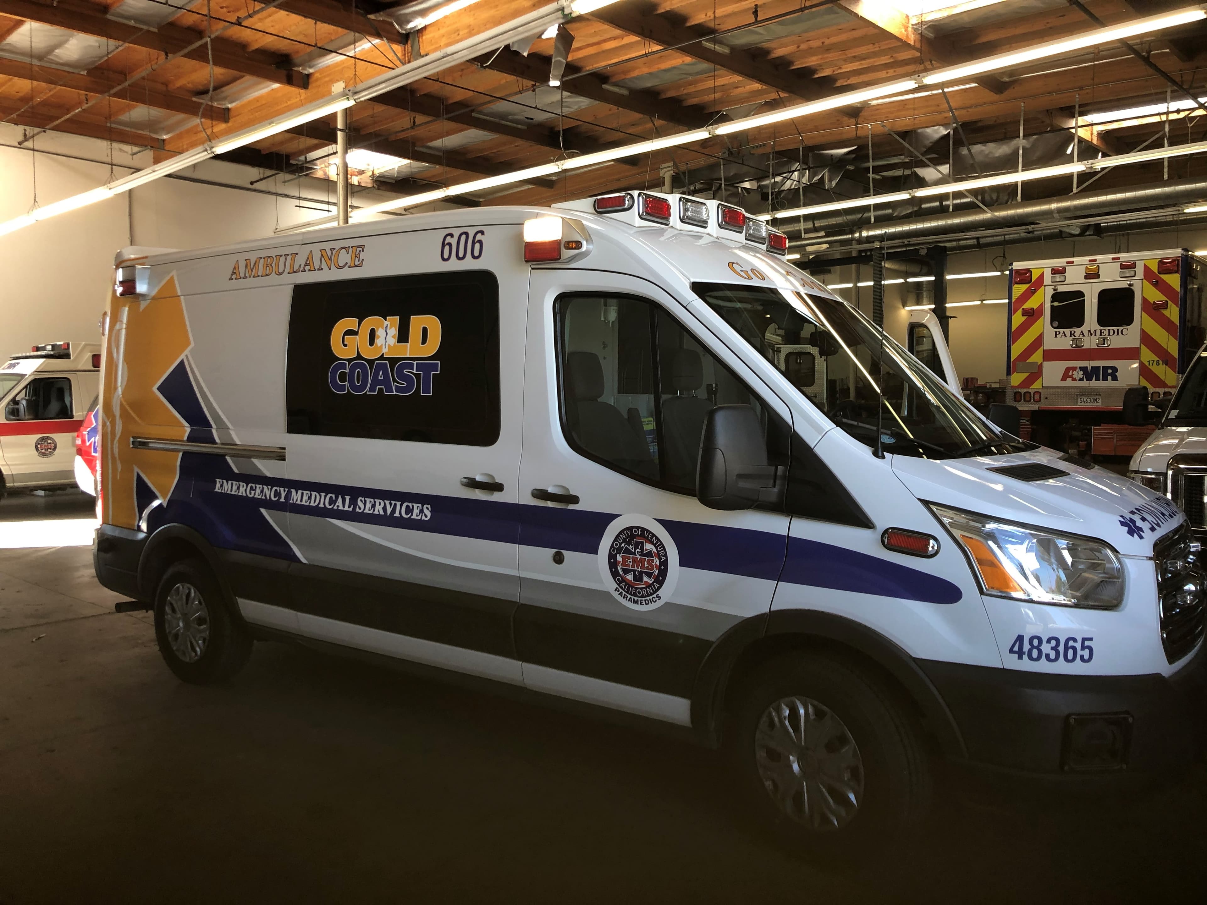 Gold Coast Ambulance Ford Transit EMS unit 606 in an apparatus bay, carrying reflective blue and gold striping, an agency seal and large unit numbering
